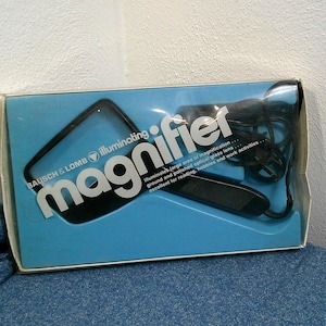 May include: A Bausch & Lomb illuminating magnifier in its original packaging. The box is blue with the word "magnifier" in large white letters. The magnifier has a black handle and a clear lens.