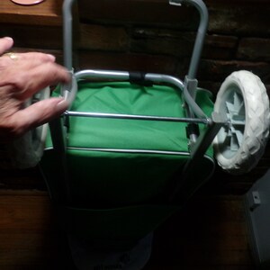 May include: A green folding wagon with a silver frame and two white wheels. The wagon is folded and has a handle.
