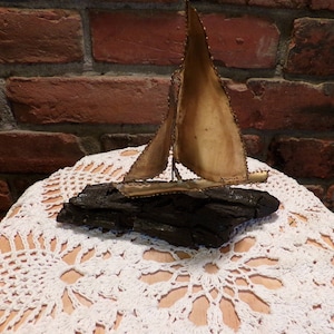 May include: A gold metal sailboat sculpture on a dark wood base. The sculpture is sitting on a white crocheted doily.