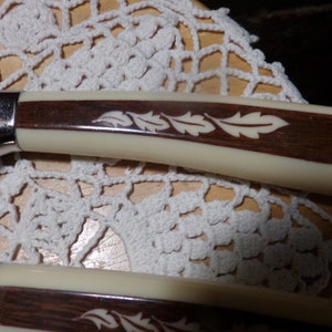 Puede incluir: Dos cuchillos de cocina con mangos de madera marrón e insertos de plástico blanco. Los mangos tienen un diseño decorativo de hojas.