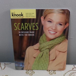 May include: A book cover with the title "SCARVES" in green lettering. The book features a woman wearing a green scarf. The text "NOW YOU CAN KNIT WITH A CROCHET HOOK!" is also visible. The book is titled "the knook".