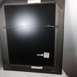 May include: A black wood picture frame with a black mat and a wire hanging system. The frame has a label on the back.