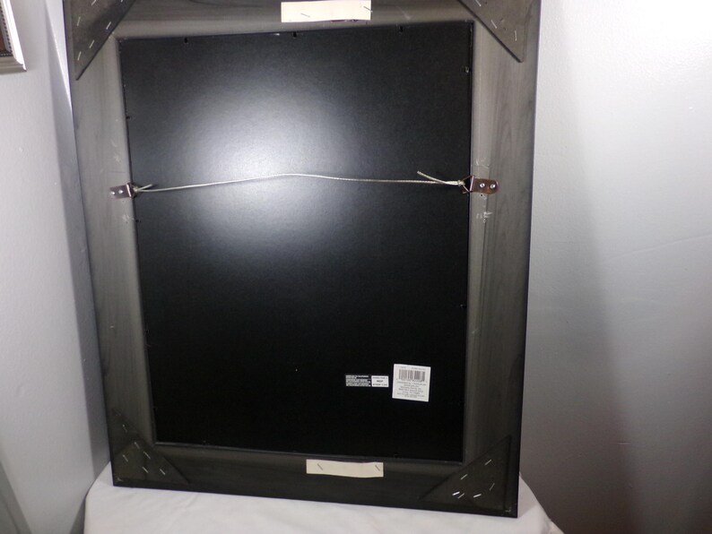 May include: A black wood picture frame with a black mat and a wire hanging system. The frame has a label on the back.