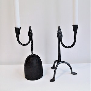 May include: Two black metal candle holders with white candles. One holder has a round base and the other has three legs.