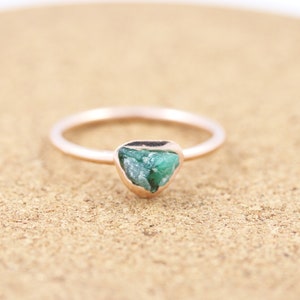 May include: A rose gold ring with a raw emerald gemstone set in the center.