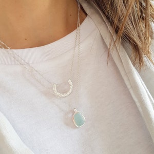 May include: A silver necklace with a twisted silver pendant and a light blue stone pendant.