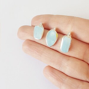 May include: Three silver pendants with light blue aquamarine stones. The stones are different shapes, including a rectangle, oval, and a slightly rounded rectangle.