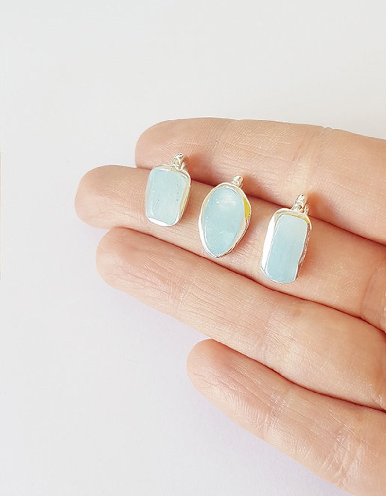 May include: Three silver pendants with light blue aquamarine stones. The stones are different shapes, including a rectangle, oval, and a slightly rounded rectangle.