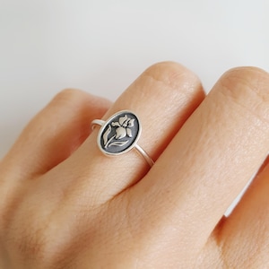 Puede incluir: Un anillo de plata con un diseño ovalado que presenta un motivo floral en blanco y negro.