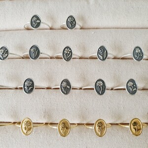 Pu&ograve; includere: Una esposizione di anelli in argento e oro con motivi floreali. Gli anelli sono disposti in file su uno sfondo di tessuto bianco.