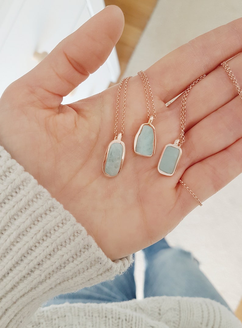 May include: Three delicate necklaces with light blue stone pendants set in rose gold. The stones are irregular in shape and have a smooth, polished finish.