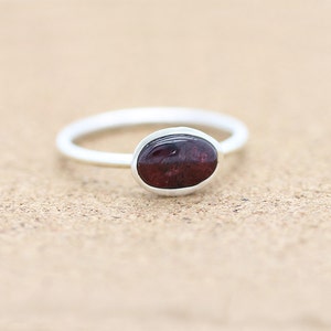 May include: A silver ring with a dark red oval gemstone.