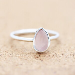 Op de afbeelding: Een zilveren ring met een traanvormige roze rozenkwarts steen.