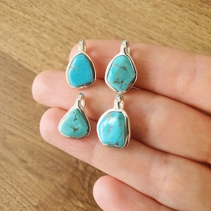 Op de afbeelding: Vier turquoise edelsteen hangers met zilveren instellingen. De stenen zijn in verschillende vormen en maten.