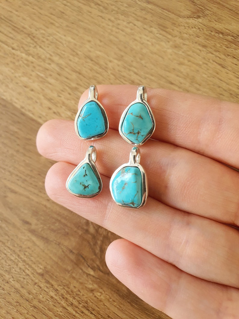 Op de afbeelding: Vier turquoise edelsteen hangers met zilveren instellingen. De stenen zijn in verschillende vormen en maten.