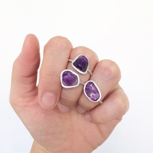 Könnte beinhalten: Drei Silberringe mit Amethyst-Edelsteinen. Die Ringe werden an einer Hand getragen, wobei der größte Ring am Zeigefinger, der mittlere Ring am Mittelfinger und der kleinste Ring am Ringfinger sitzt.