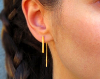 May include: A pair of gold bar earrings with a long, thin, straight bar hanging from each earring.