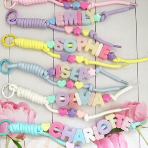 May include: Six personalized lanyards featuring pastel-colored silicone letter beads spelling the names AVA, EMILY, SOPHIE, ISLA, OLIVIA, and CHARLOTTE. Each lanyard includes a metal clasp, a knotted cord, and decorative heart and star-shaped beads.