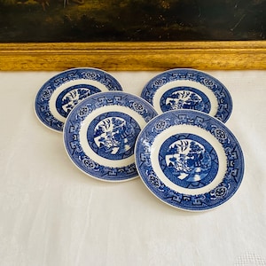 May include: Four blue and white porcelain plates with a traditional willow pattern. The plates have a white background with a blue border and a blue willow tree design in the center.