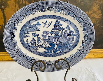 May include: A blue and white oval ceramic serving platter with a willow tree design. The platter is on a metal stand.