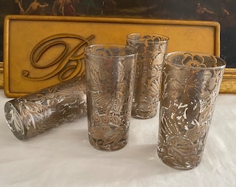 May include: Set of four clear glass tumblers with a gold floral pattern. The glasses are tall and slender, with a slightly flared rim.
