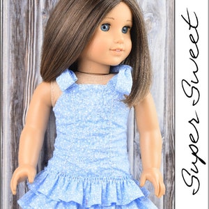 May include: A blue and white floral print dress with a ruffled hem. The dress has a halter style neckline with two bows on the straps. The dress is designed for a doll.