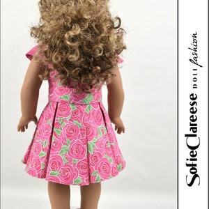 May include: A pink dress with a floral print of roses and green leaves. The dress has a pleated skirt and short sleeves. The dress is being worn by a doll with long curly brown hair.