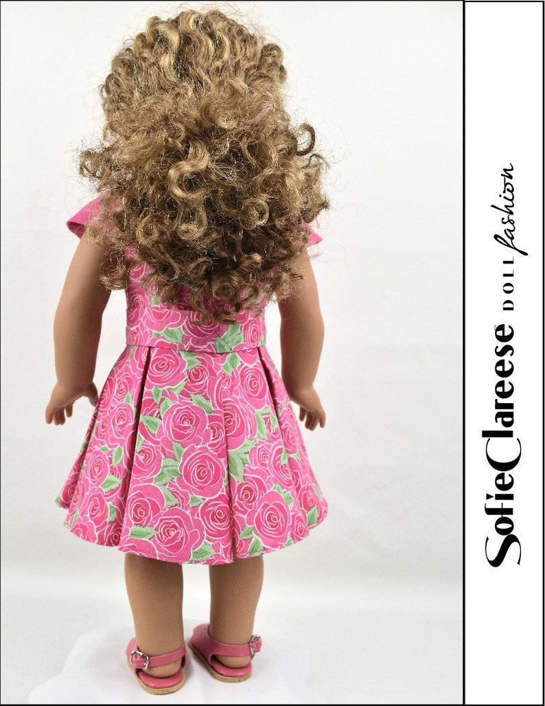 May include: A pink dress with a floral print of roses and green leaves. The dress has a pleated skirt and short sleeves. The dress is being worn by a doll with long curly brown hair.