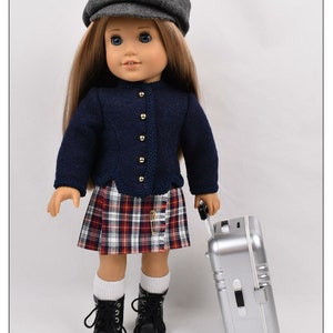 May include: A doll wearing a blue sweater, plaid skirt, black boots, and a gray newsboy cap. The doll is holding a silver suitcase with wheels.