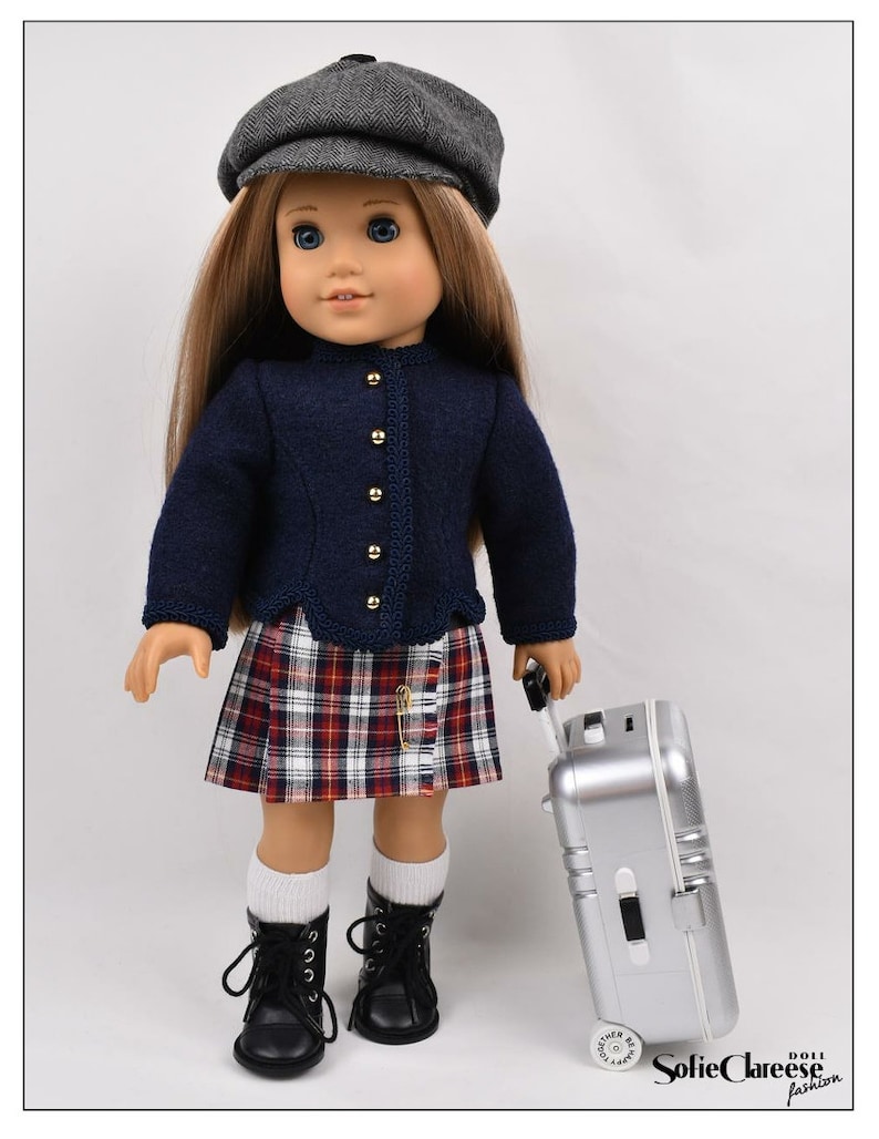 May include: A doll wearing a blue sweater, plaid skirt, black boots, and a gray newsboy cap. The doll is holding a silver suitcase with wheels.