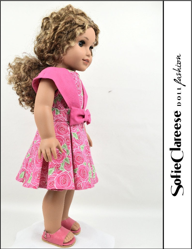 May include: A pink dress with a floral print and a matching pink bow. The dress has short sleeves and a full skirt. The doll is wearing pink sandals.