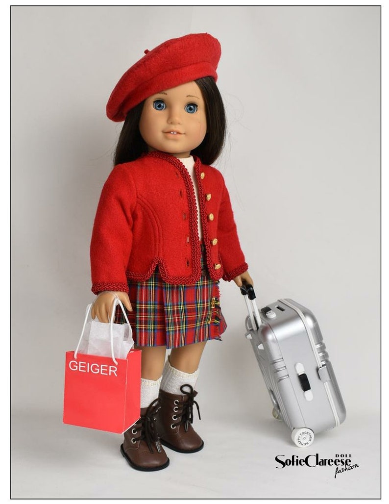 May include: A red beret, red jacket, and plaid skirt outfit for a doll. The doll is holding a red shopping bag with the word "GEIGER" printed on it and a silver suitcase with wheels.