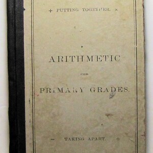 Puede incluir: Una portada de libro vintage con el título "Arithmetic for Primary Grades". La portada es beige con texto negro y un borde negro. El texto en la portada dice "Putting Together" y "Taking Apart".
