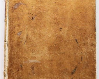 Pode incluir: Um livro antigo com uma capa de couro desgastada. A capa é de cor castanho claro com manchas e marcas mais escuras, indicando idade e uso. A lombada mostra as páginas envelhecidas, esbranquiçadas.