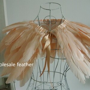 May include: A peach-colored feather shawl with a satin ribbon tie. The shawl is displayed on a wire mannequin.