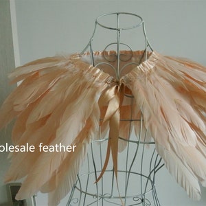 May include: A peach-colored feather shawl with a satin ribbon tie. The shawl is displayed on a wire mannequin.