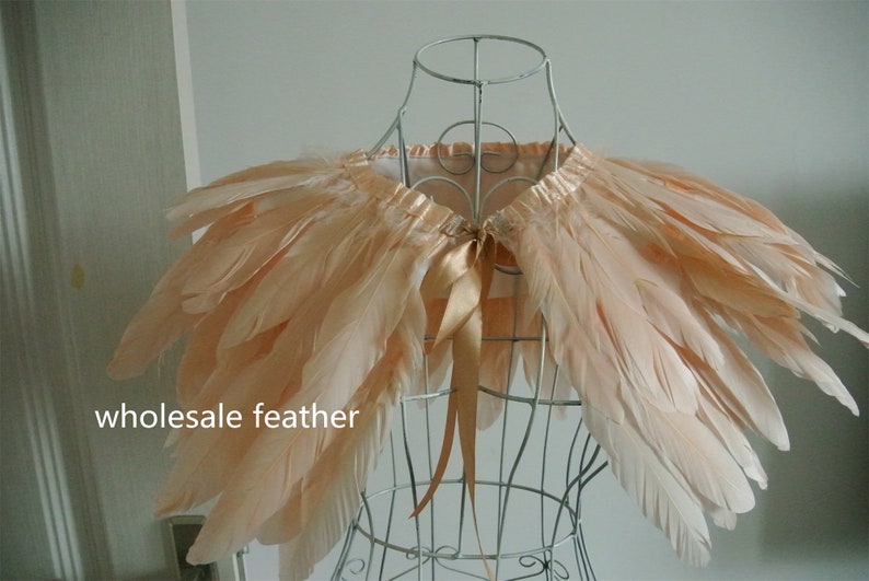 May include: A peach-colored feather shawl with a satin ribbon tie. The shawl is displayed on a wire mannequin.
