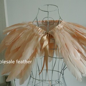 May include: A peach-colored feather boa with a satin ribbon tie. The boa is displayed on a wire mannequin. "wholesale feather" is written in the bottom left corner of the image.