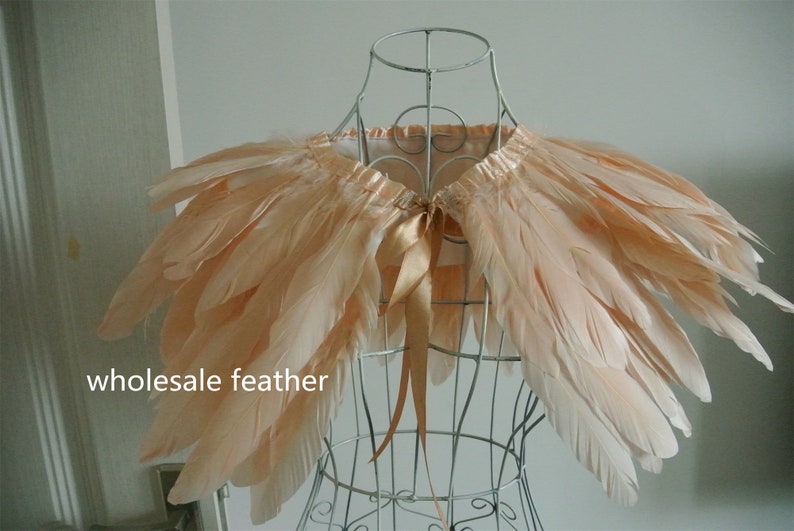 May include: A peach-colored feather boa with a satin ribbon tie. The boa is displayed on a wire mannequin. "wholesale feather" is written in the bottom left corner of the image.