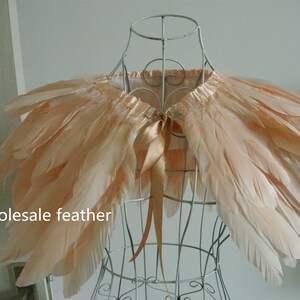May include: A peach-colored feather shawl with a satin ribbon tie. The shawl is displayed on a wire mannequin.