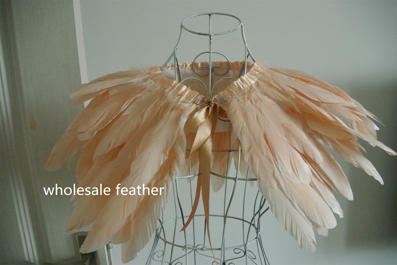 May include: A peach-colored feather shawl with a satin ribbon tie. The shawl is displayed on a wire mannequin.