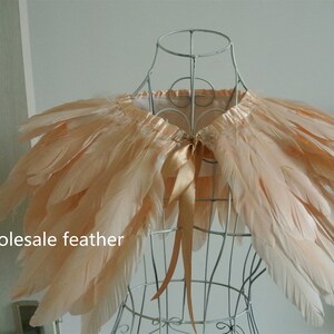 May include: A peach-colored feather cape with a satin ribbon tie. The cape is displayed on a wire mannequin.