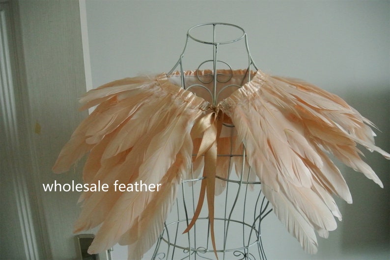 May include: A peach-colored feather cape with a satin ribbon tie. The cape is displayed on a wire mannequin.