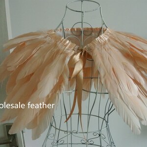 May include: A peach-colored feather shawl with a satin ribbon tie. The shawl is displayed on a wire mannequin.