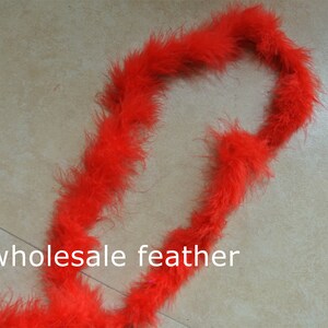 Pode incluir: Uma longa fita de boa de penas vermelho brilhante. A boa está enrolada em forma de círculo. O texto "wholesale feather" é visível na imagem.