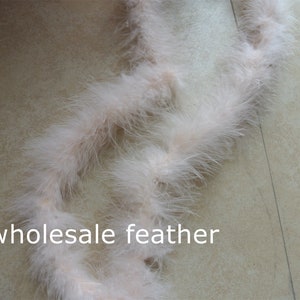 Op de afbeelding: Een lange streng zachte, witte verenboa. De boa is gekruld en gedraaid, waardoor de pluche textuur zichtbaar is. De tekst "wholesale feather" is zichtbaar in de linkerbenedenhoek van de afbeelding.