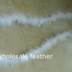 May include: A long strand of white feather boa. The boa is lying on a light brown surface. The text "wholesale feather" is visible in the bottom centre of the image.