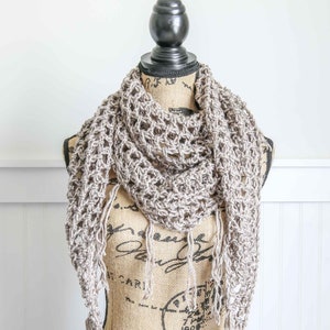 May include: A crocheted scarf in a light brown color with fringe on the ends. The scarf is draped over a burlap mannequin.