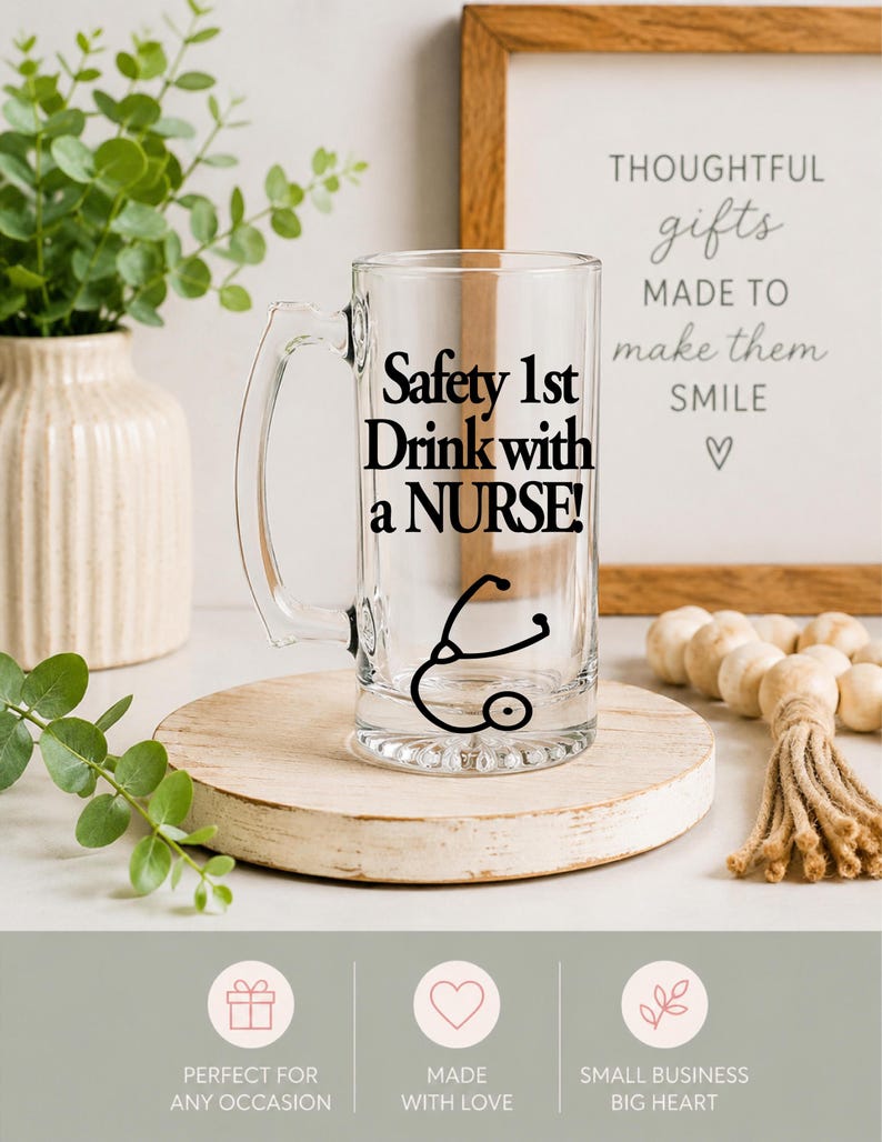 May include: A clear glass beer mug with a handle, featuring the text "Safety 1st Drink with a NURSE!" in black. A black stethoscope graphic is below the text. The mug sits on a wooden round stand, with a framed sign in the background.