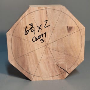 Puede incluir: Un bloque octogonal de madera de cerezo marrón claro, con un círculo de lápiz y líneas radiales. El bloque está etiquetado con las medidas "6 3/4 x 2" y la palabra "Cherry" con el número "3" debajo.
